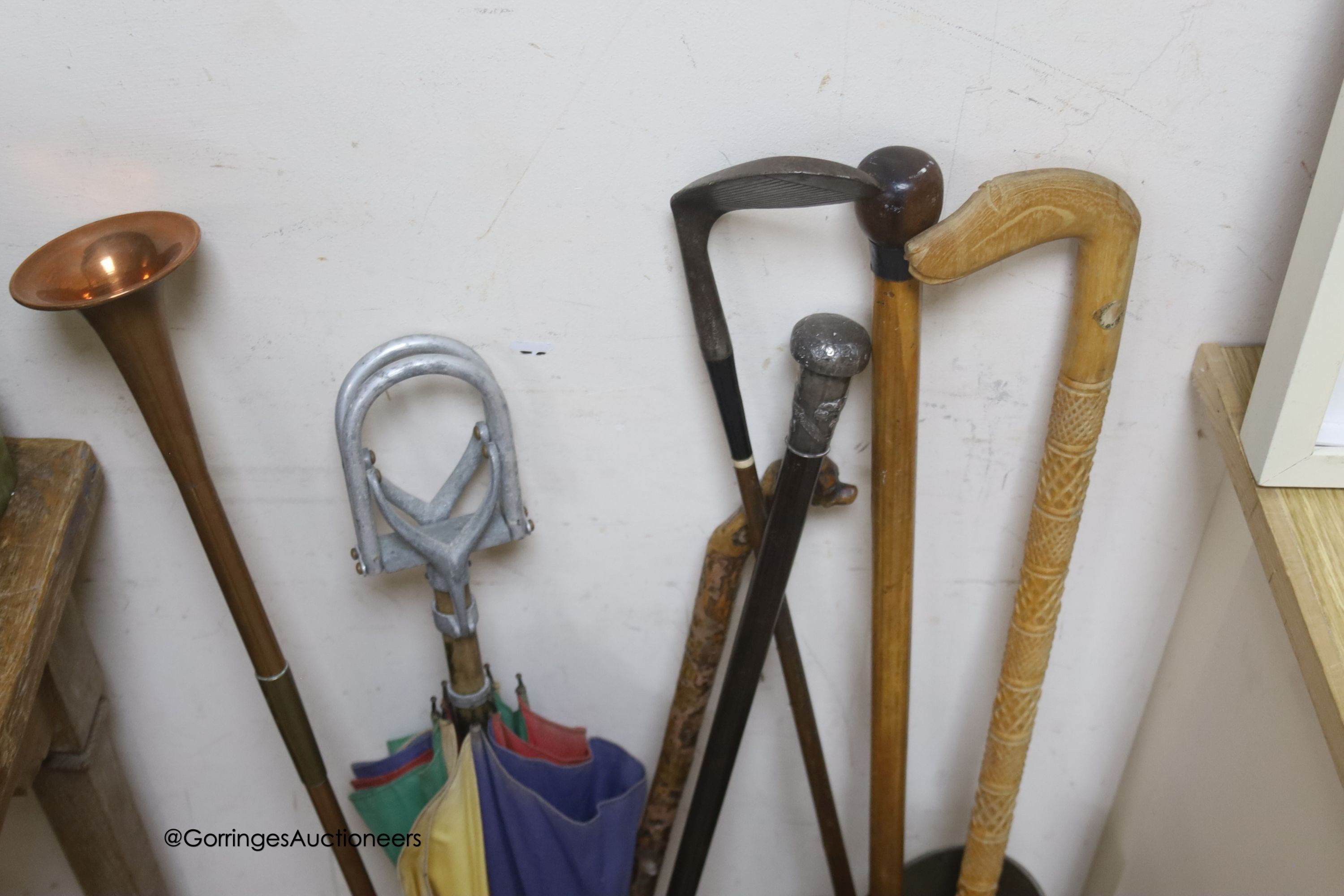 A Chinese white metal topped cane hunting horn, dog head cane, shooting stick and a Japanese embossed shell case, walking sticks, a golfing putt and a boot shaped umbrella stand